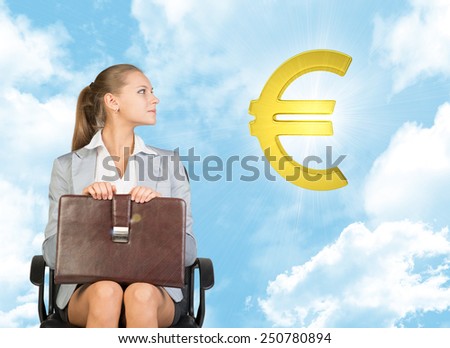Businesswoman sitting on office chair, holding briefcase on her knees, looking up at golden euro sign in the air, against blue sky with clouds