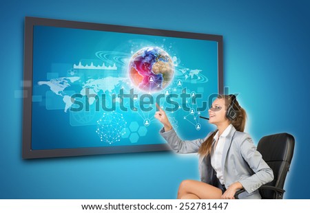 Businesswoman in headset using touch screen interface with Globe, network of person icons and other elements, on blue background. Element of this image furnished by NASA