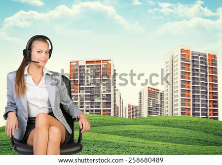 Woman in jacket and blouse with headphones sits on chair. Buildings and green hills in background