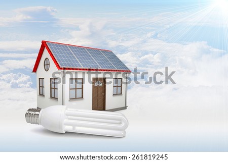 White house with red roof, brown door and solar panels in clouds. Background sun shines brightly on large clouds