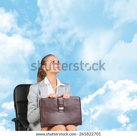 Business woman in skirt, blouse and jacket, sitting on chair and holding briefcase. Against background of blue sky and clouds