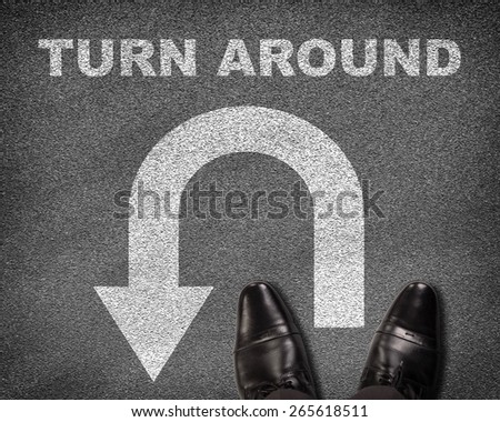 Top view of shoes standing on asphalt road with U-turn sign and text turn around. Business concept
