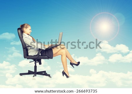 Beautiful businesswoman in suit sitting on office chair and holding open laptop, leaning back, smiling