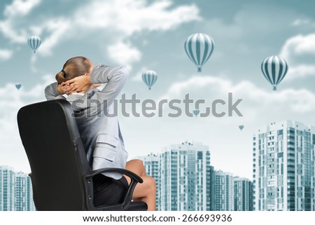 Businesswoman sitting backwards on chair relaxed and put hands behind her head. Building as backdrop