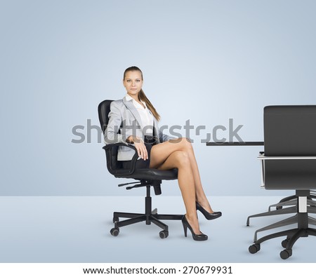 Businesslady sitting half-turned in chair with her crossed legs and looking at camera on white background. Business office.