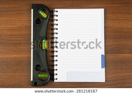Builders level with note pad on brown wooden table, top view