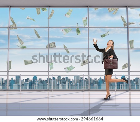 Businesswoman holding suitcase and coffee cup, looking at camera under money rain
