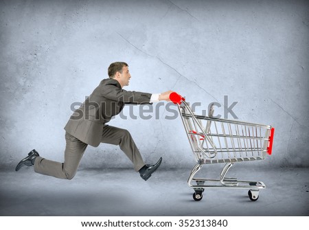 Businessman pushing shopping cart on grey wall background