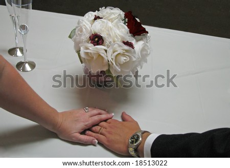 newly married couple holding hands by flowers with rings