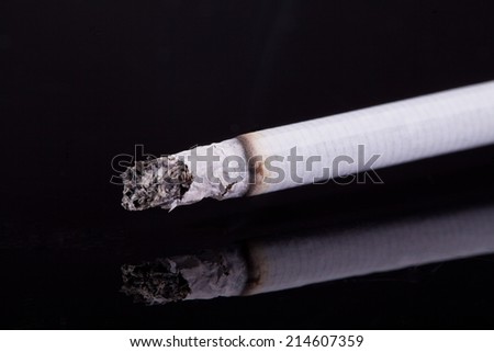 single burning cigarette with ash isolated on black background