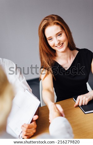 Red haired young woman shaking hands in office