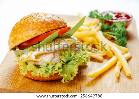 Burger with chicken, fried egg and french fries on a wooden stand