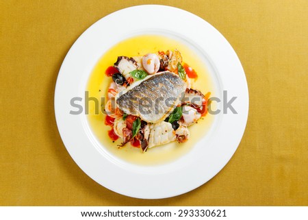 Dorado with seafood and cherry tomatoes on a white plate. Top view