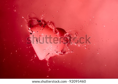 A pink heart splashing onto the surface of water with pink background.