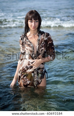 Young sexy slim brunette woman in a wet beach dress standing in ocean water. Tenerife, Spain.