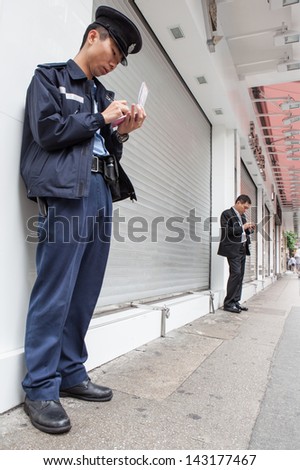 KOWLOON, HONG KONG -Â?Â? MARCH 16: Unidentified Police officer takes notes while unidentified businessman texts on smartphone in Kowloon, Hong Kong on March 16th, 2013.