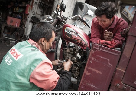FOSHAN, GUANGDONG/CHINA - MARCH 16: Unidentified garage mechanic works on motorcycle as customer watches in Shunde District of Foshan City, Guangdong Province, China on March 16th, 2013.