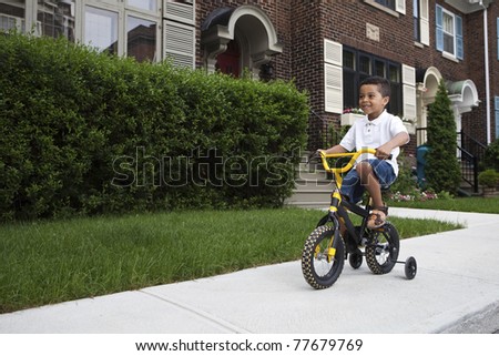 Young boy riding his first bicycle with training wheels (horizontal)