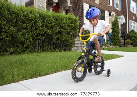 Young boy with helmet riding his first bicycle with training wheels
