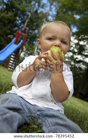 Young boy eating a green apple at the park