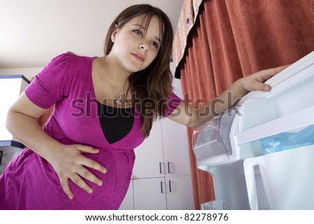 Young pregnant woman looking into refrigerator for something to eat