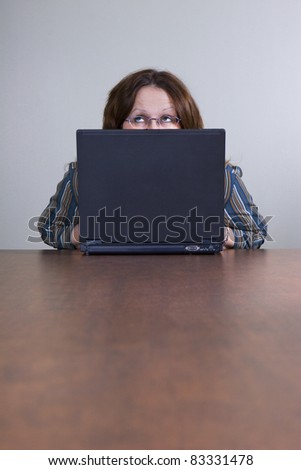 Businesswoman peeking from behind laptop