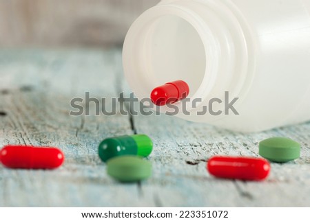 Green and red pills with bottle on old wooden table