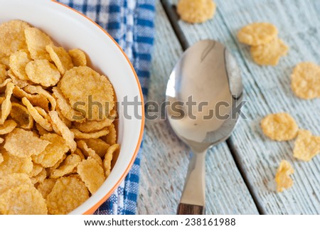 Bowl of corn flakes with spoon and towel on old wooden table