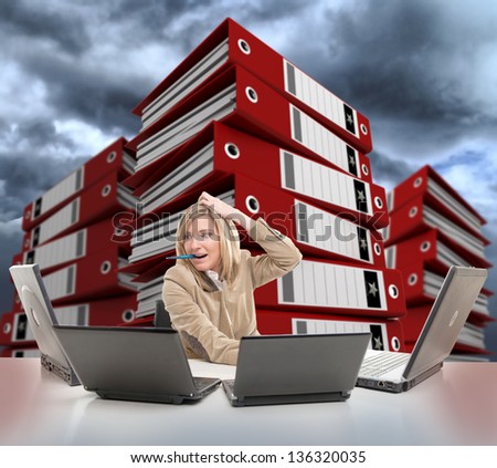 Stressed young woman using multiple computers, with piles of folders on the backgrounds