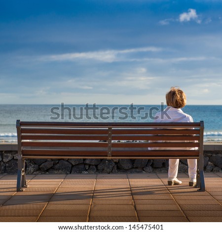 Woman sitting alone in a bench, looking at the sea