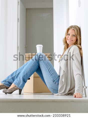 Smiling woman sitting on the floor with a pile of boxes, having a coffee break