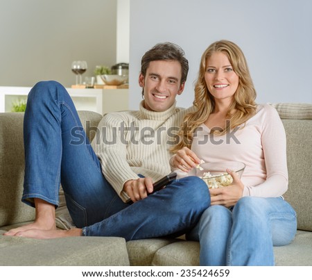 A couple after dinner watching tv with a bowl of popcorn