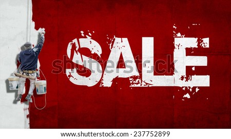 Painter hanging from harness painting a wall with the word sale