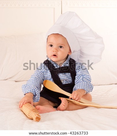 Cute baby with a cook hat playing with a rolling pin and wooden spoons