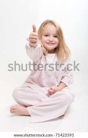 Cute little blonde girl in her pajamas sitting on the floor doing the