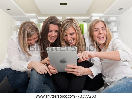 Group of girls laughing looking at a pc tablet in a modern interior. Please note that the logo and writing on the tablet are mine. I am attaching a property release, so no copyright issue.