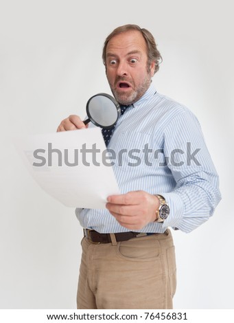 Man with a shocked expression analyzing a document through a magnifying glass