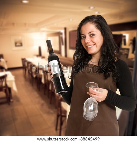 Smiling female sommelier presenting a wine bottle with a blank label and a pair of glasses in a restaurant