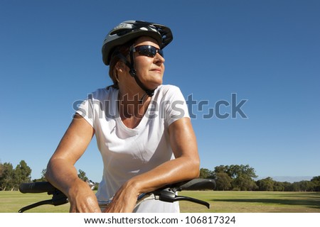 Portrait Fit and healthy looking mature woman in her fifties riding her bike, isolated with park and blue sky as background and copy space.