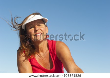 Portrait of happy attractive looking middle aged woman joyful laughing, isolated with sunshine on face and blue sky as background and copy space.