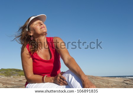 Portrait of happy attractive looking middle aged woman joyful laughing, isolated with sunshine on face, ocean and blue sky as background and copy space.