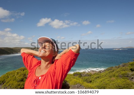Portrait of happy attractive looking mature middle aged woman joyful laughing, isolated with sunshine on face, ocean, sly and coastline as background and copy space.