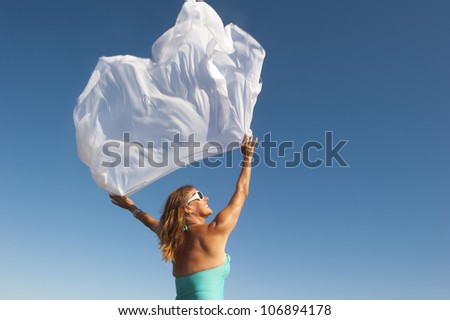 Happy and joyful attractive middle aged woman holding fluttering white cloth in the wind, isolated with blue sky as background and copy space.