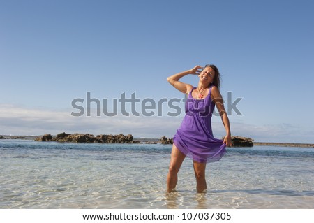 Pretty looking mature woman in sexy purple dress  at tropical beach, with ocean and blue sky as background and copy space.