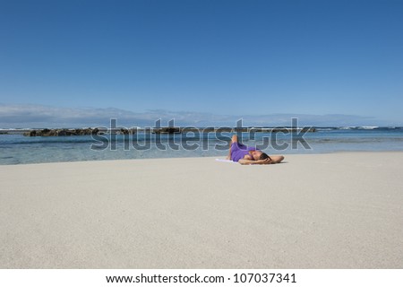 Pretty looking mature woman in sexy purple dress and high heel shoes at the beach, with ocean and blue sky as background and copy space.