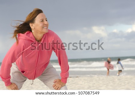 Portrait of confident, healthy and sporty fit attractive looking mature woman in pink sweater, at beach, isolated with storm clouds and ocean as background and copy space.