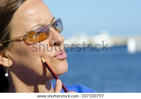 Portrait mature woman outdoor in thinking pose, with pen in one hand, isolated with blurred background as copy space.