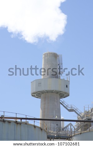 Smoke coming out of towering chimney at factory plant, as a symbol for industrial pollution of environment, isolated with blue sky as background and copy space.