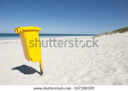 Bright yellow colored rubbish bin at remote tropical beach, to keep environment clean, isolated with ocean and blue sky as background and copy space.