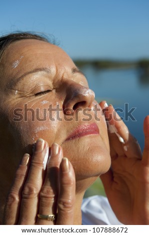 Portrait of attractive mature woman with suncream on her face to protect herself from skin cancer, isolated with blurred background and copy space.